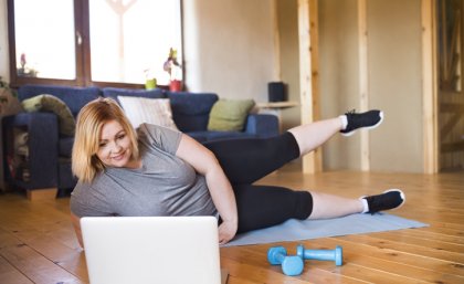 woman in exercise gear lying on a yoga mat in front of a lap top, doing scissor kicks